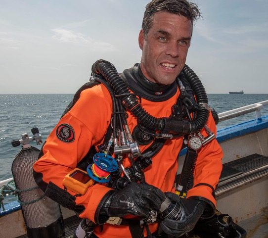Bas Poelmann in oranje droogpak op een boot Bas Poelmann in oranje droogpak op een boot
