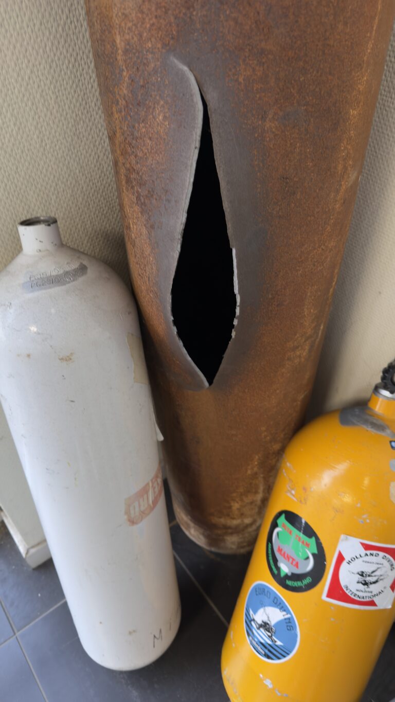 Doorgeroeste stalen duikfles met een scheur in de wand, gezien bij een keuringsbedrijf
